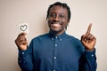 African american romantic man holding reminder with heart symbol over white background surprised with an idea or question pointing Royalty Free Stock Photo