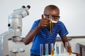 African american schoolboy in safety glasses and face mask looking at test tubes in science class