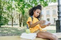 African american schoolgirl sitting on bench near books and using smartphone Royalty Free Stock Photo