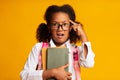 African American Schoolgirl Twisting Finger At Temple, Yellow Background