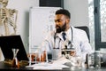 African american scientist doctor in white coat working with microscope, test tubes in laboratory, making notes on