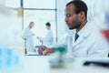 African american scientist in white coat taking notes while working in laboratory