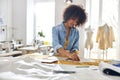 African-American seamstress works with sewing patterns and yellow fabric at cutting table