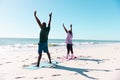 African american senior couple with arms raised exercising on mats at beach under clear blue sk Royalty Free Stock Photo