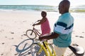 African american senior couple with bikes talking and walking on sandy beach against sky in summer Royalty Free Stock Photo