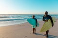 African american senior couple carrying surfboards while walking at sandy beach against sky Royalty Free Stock Photo