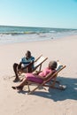 African american senior couple sitting on deckchairs and talking at beach under clear sky in summer Royalty Free Stock Photo