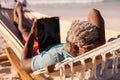 African american senior man with gray hair using digital tablet while lying on hammock at beach Royalty Free Stock Photo