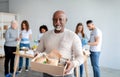 African american senior man holding box with donations food, looking and smiling at camera in charity center Royalty Free Stock Photo