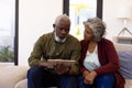 African american senior man using digital tablet while sitting with woman on sofa in nursing home Royalty Free Stock Photo