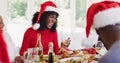 African american senior man and young woman in santa hats talking and smiling while sitting on dinin