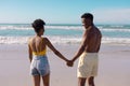 African american shirtless young man holding woman\'s hands while standing at beach against sky Royalty Free Stock Photo