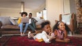 African American sibling lying on floor and watching television while parents using laptop on sofa Royalty Free Stock Photo