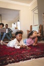 African American sibling lying on floor and watching television while parents using laptop on sofa Royalty Free Stock Photo