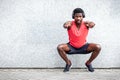 African american sports guy working out with headphones outdoors against wall, athletic man crouches and does physical exercises