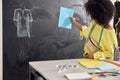 African-American teacher shows blank blue paper against blackboard at sewing class Royalty Free Stock Photo