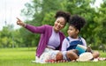 African American teacher is teaching her young student to read while having a summer outdoor class in the public park for Royalty Free Stock Photo