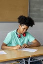 African american teen boy high school student sitting behind desk in classroom doing homework. Vertical image Royalty Free Stock Photo