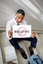 African-American teenage boy holding sheet of paper with word BULLYING at school