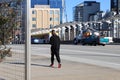 An African American teenager in a black and red sweat suit walking along the sidewalk with cars driving and office buildings