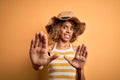 African american tourist woman with curly on vacation wearing summer hat and striped t-shirt afraid and terrified with fear