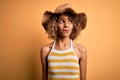 African american tourist woman with curly on vacation wearing summer hat and striped t-shirt smiling looking to the side and Royalty Free Stock Photo