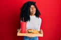 African american woman with afro hair eating a tasty classic burger with fries and soda smiling looking to the side and staring Royalty Free Stock Photo