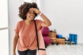 African american woman with afro hair holding yoga mat at pilates room very happy and smiling looking far away with hand over head Royalty Free Stock Photo