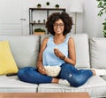 African american woman with afro hair sitting on the sofa eating popcorn at home looking positive and happy standing and smiling Royalty Free Stock Photo