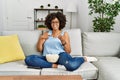 African american woman with afro hair sitting on the sofa eating popcorn at home smiling happy pointing with hand and finger Royalty Free Stock Photo