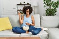 African american woman with afro hair sitting on the sofa eating popcorn at home smiling happy pointing with hand and finger to Royalty Free Stock Photo