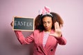 African american woman with afro hair wearing bunny ears holding blackboard with message with open hand doing stop sign with