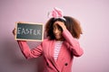 African american woman with afro hair wearing bunny ears holding blackboard with message stressed with hand on head, shocked with