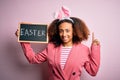 African american woman with afro hair wearing bunny ears holding blackboard with message surprised with an idea or question