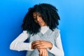 African american woman with afro hair wearing casual winter sweater checking the time on wrist watch, relaxed and confident Royalty Free Stock Photo