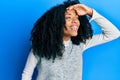 African american woman with afro hair wearing casual winter sweater very happy and smiling looking far away with hand over head Royalty Free Stock Photo