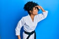 African american woman with afro hair wearing karate kimono and black belt very happy and smiling looking far away with hand over Royalty Free Stock Photo