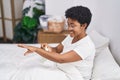 African american woman applying cream treatment sitting on bed at bedroom Royalty Free Stock Photo