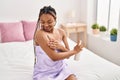 African american woman applying skin treatment sitting on bed at bedroom Royalty Free Stock Photo