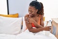 African american woman applying skin treatment sitting on bed at bedroom Royalty Free Stock Photo