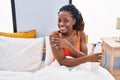African american woman applying skin treatment sitting on bed at bedroom Royalty Free Stock Photo