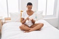 African american woman applying skin treatment sitting on bed at bedroom Royalty Free Stock Photo