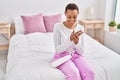 African american woman applying skin treatment sitting on bed at bedroom Royalty Free Stock Photo