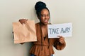 African american woman with braided hair holding take away paper bag in shock face, looking skeptical and sarcastic, surprised Royalty Free Stock Photo