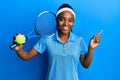 African american woman with braided hair playing tennis holding racket and ball smiling happy pointing with hand and finger to the Royalty Free Stock Photo
