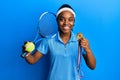 African american woman with braided hair playing tennis holding racket and ball and winner medal smiling with a happy and cool Royalty Free Stock Photo