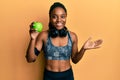 African american woman with braided hair wearing sportswear and headphones eating green apple celebrating achievement with happy Royalty Free Stock Photo