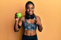 African american woman with braided hair wearing sportswear and headphones eating green apple smiling happy pointing with hand and Royalty Free Stock Photo