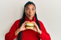 African american woman with braids eating hamburger making fish face with mouth and squinting eyes, crazy and comical