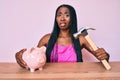 African american woman with braids holding piggy bank and hammer clueless and confused expression Royalty Free Stock Photo